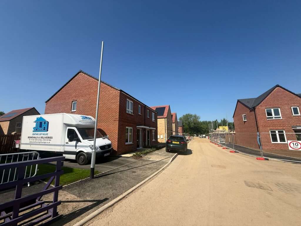 Residential Street Under Construction with Brick Townhouses on Both Sides and a White Delivery Van Parked Near the Curb on a Sunny Day