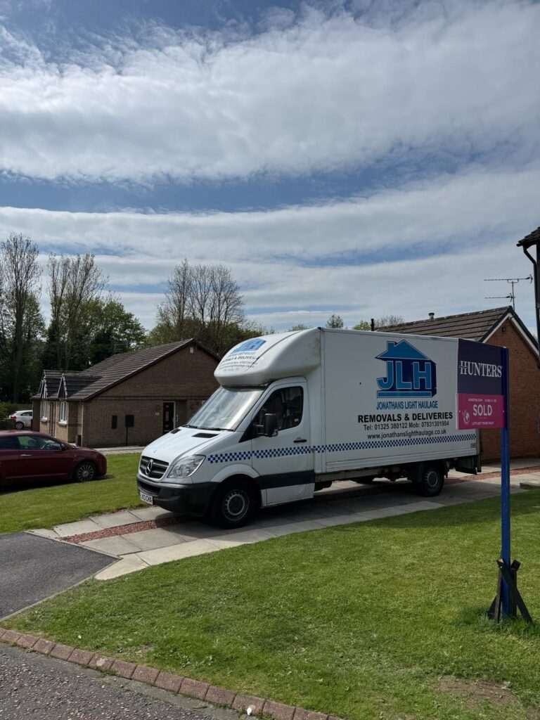 White Delivery Truck with Jlh Branding Parked on a Suburban Street, House and Green Lawn in Background, Blue Sky with Clouds